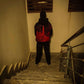 Person wearing a red and black jacket walking down a dimly lit staircase.