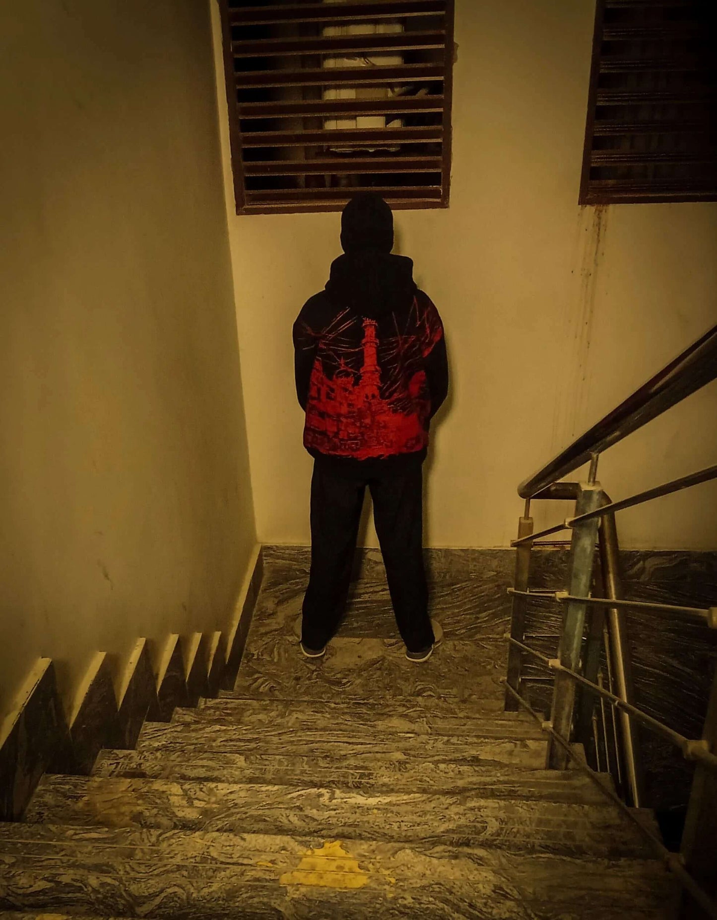 Person wearing a red and black jacket walking down a dimly lit staircase.